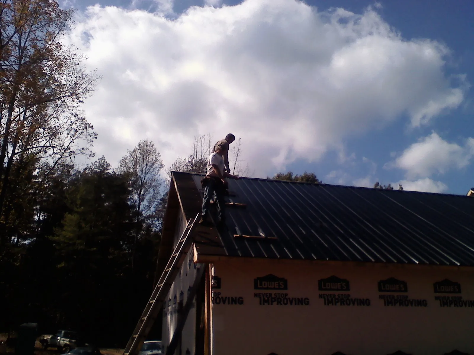 Roofer fastening dark metal panels high against a cloudy sky, from a Roof Inspection job in Kirkville